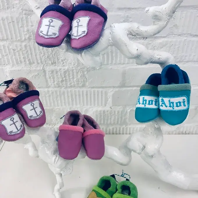 Verschiedene handgemachte Lederpuschen für Babys in maritimen Designs und bunten Farben auf einem dekorativen Astständer.