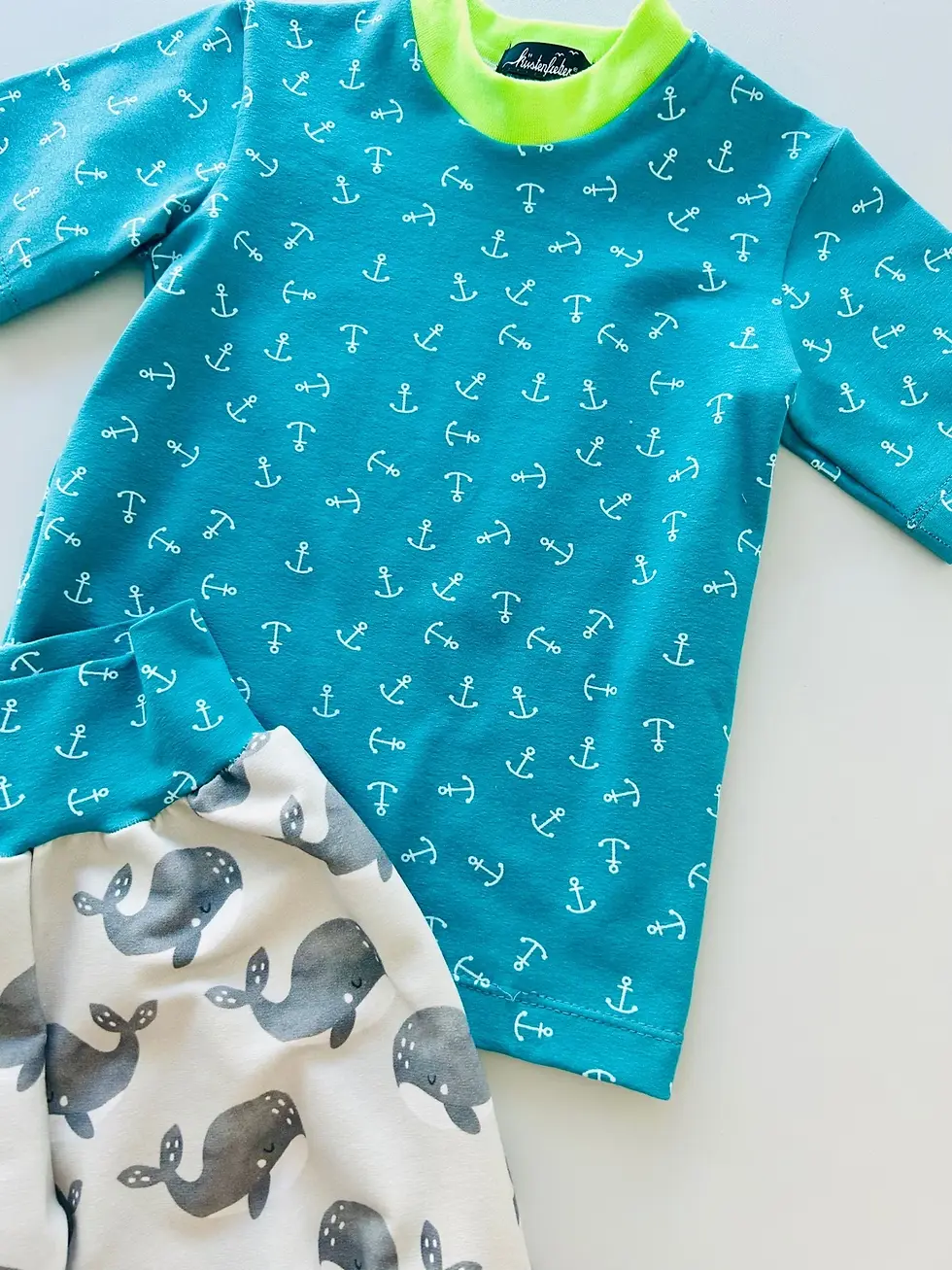 Miniaturbild: Nahaufnahme des Küstenfieber® Labels am maritimen Anker-Shirt mit limettengrünem Halsausschnitt