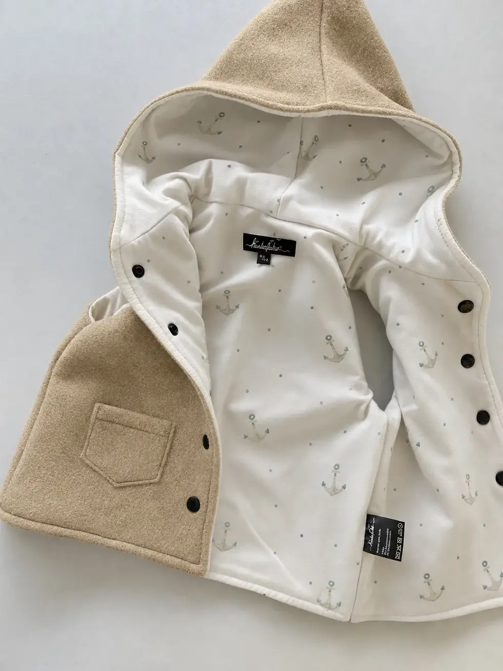 Beige Walkweste mit Kapuze für Babys und Kinder aus Wollwalk, vollständig gefüttert mit hellem Baumwolljersey mit Ankern.