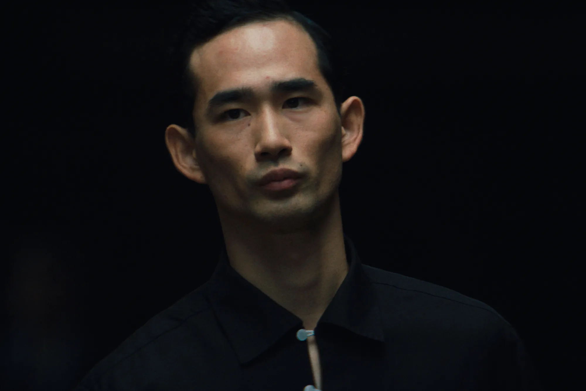 Stern looking Japanese man with sunken cheeks staring straight ahead in a dark background.
