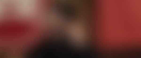 Japanese man wearing a dark jacket against a background with red posters is placing an earpiece in his ear.