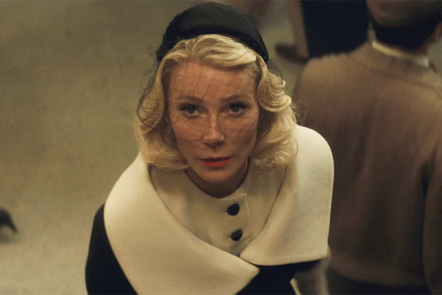 A middle aged woman with blonde hair is dressed in an elegant coat with a wide cream collar.