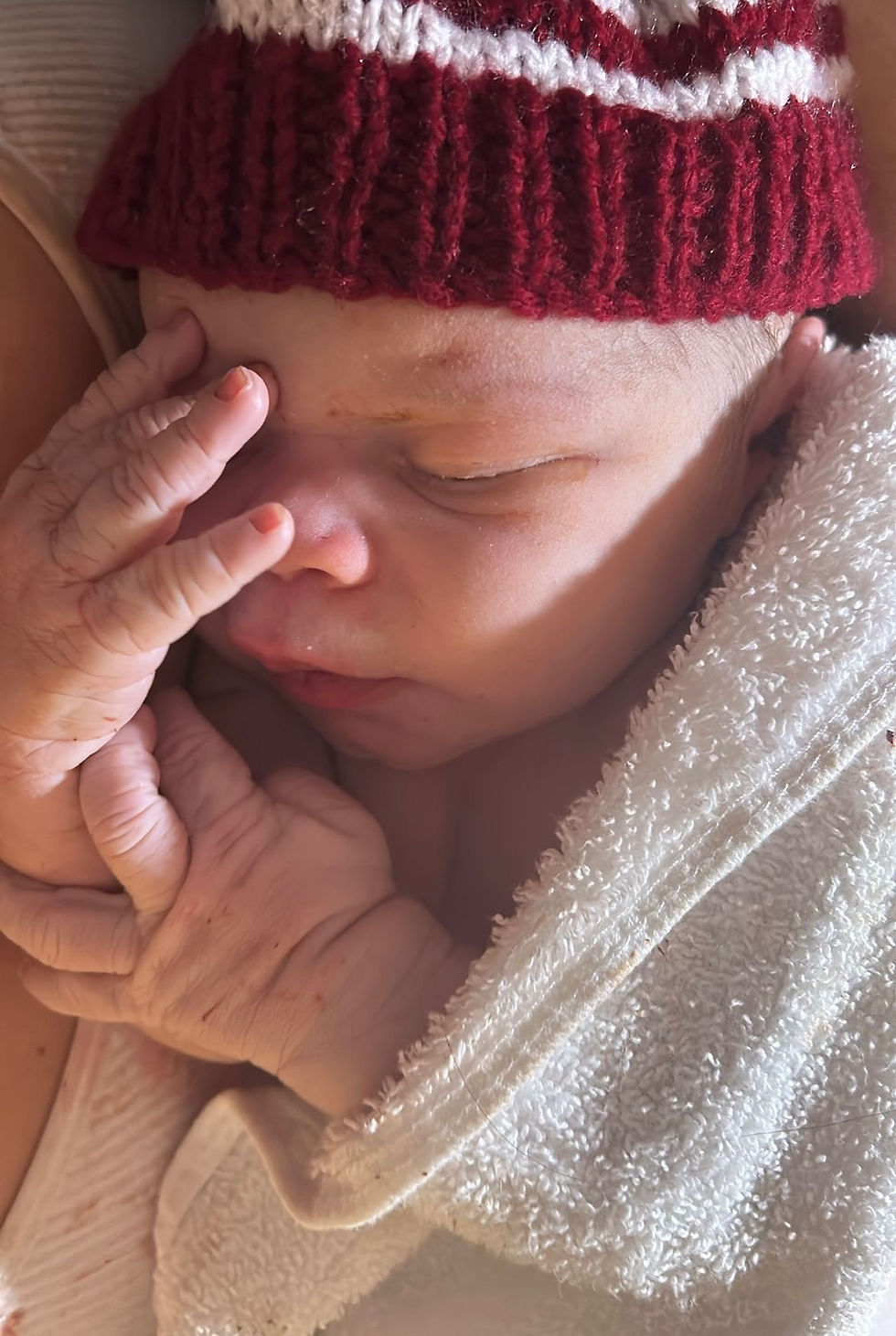 Newborn baby Dace with hand by his face wearing a hat