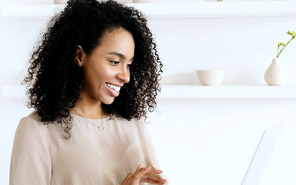 A woman holding a laptop, smiling at the content on screen