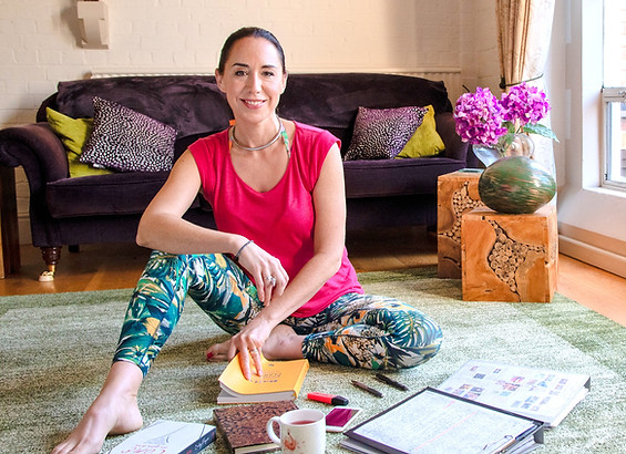 Ruth Ramsay, Adult Sex Educator and Coach, wearing a pink top and green leggings, sitting on the lounge floor surrounded by her diary and books