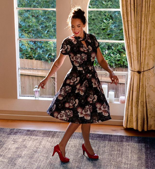 Ruth Ramsay, Adult Sex Educator and Coach, in a blue flowery dress and red high heals twirling on a rug