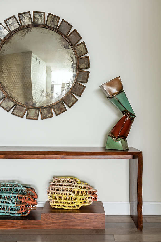 Foyer console with sculptural mirror and colorful accessories at Juliet West