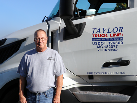 Taylor Truck Line driver Frank Goodman standing in front of his truck with the Taylor Truck Line logo on the door