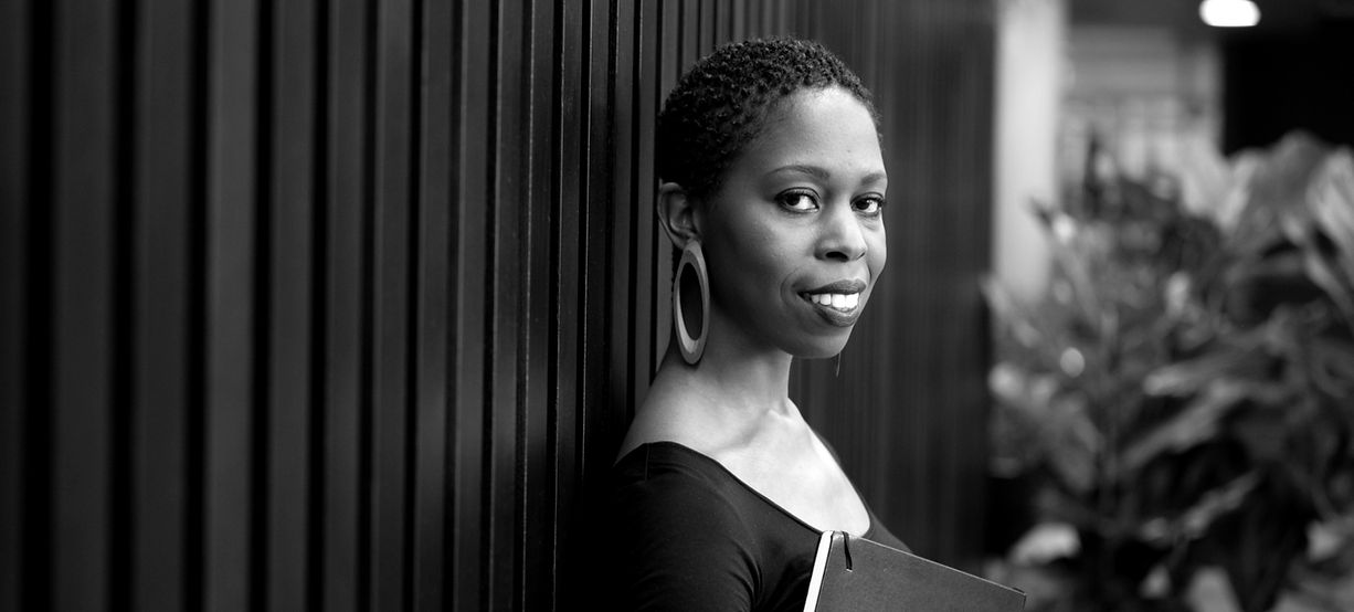 Black and white photo of Dr. Samantha Ege standing and holding a book