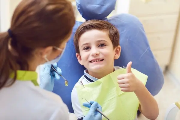 Young patient holding up a thumbs up at the dentist’s office.