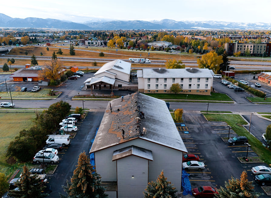 Crew mid demo proess, removing first layers of shingles on tis commercial roof. Bozeman downtown and i-90 in the background.