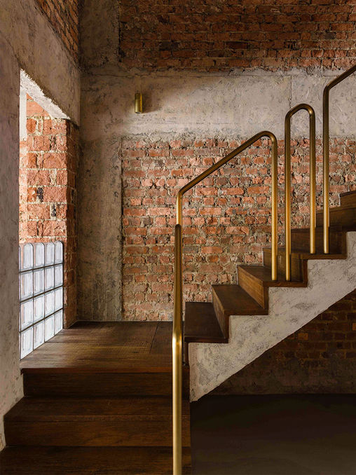 Industrial staircase with dark timber steps and brass railing against exposed brick walls