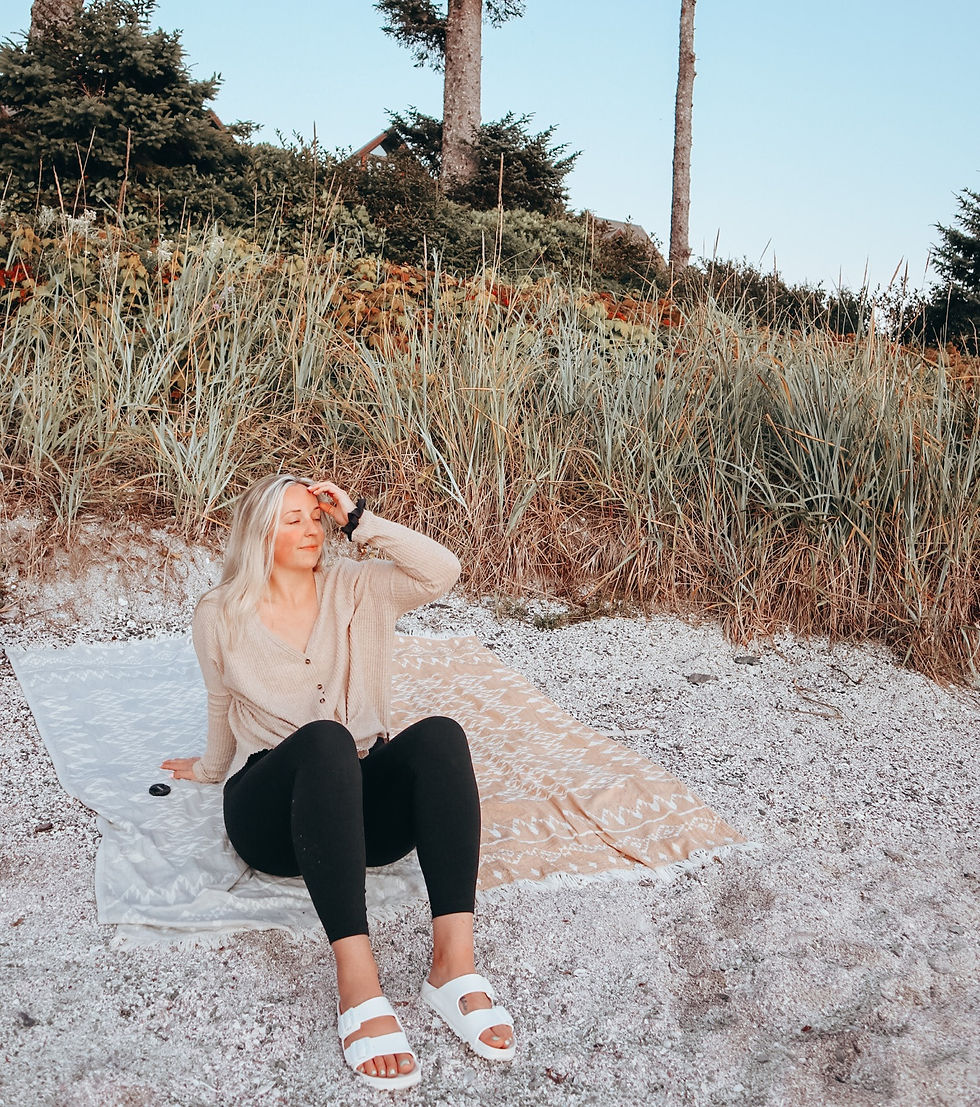 Vancouver Blogger, Taylor White, sitting on the beach in Ucluelet, BC. Wearing white birkenstocks, yoga pants and sitting on a Tofino Towel Co. Towel.