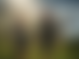 A man and woman wearing waterproof jackets and backpacks hike with trekking poles along a green coastal path as sunbeams break through dramatic rain clouds