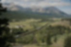 A bird's eye view reveals a long train of rail cars passing through the foothills of of Alberta Sout