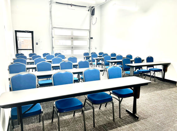 A room with several long tables with blue chairs