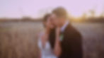 A newlywed couple embraces in a field at sunset.