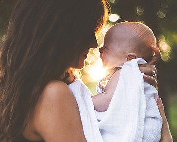 A mother who sticks her baby, nose to nose with a lot of affection. They are outside and we can see beautiful rays of sunshine behind them.