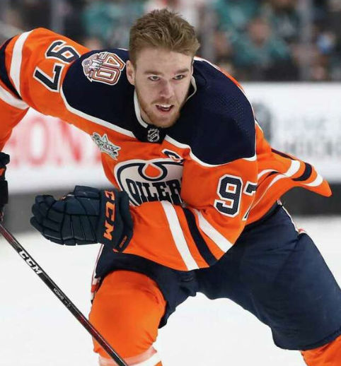 ChatGPT said:  Hockey player in an orange uniform skating with the puck, showing strong edge control and low athletic posture during game play.