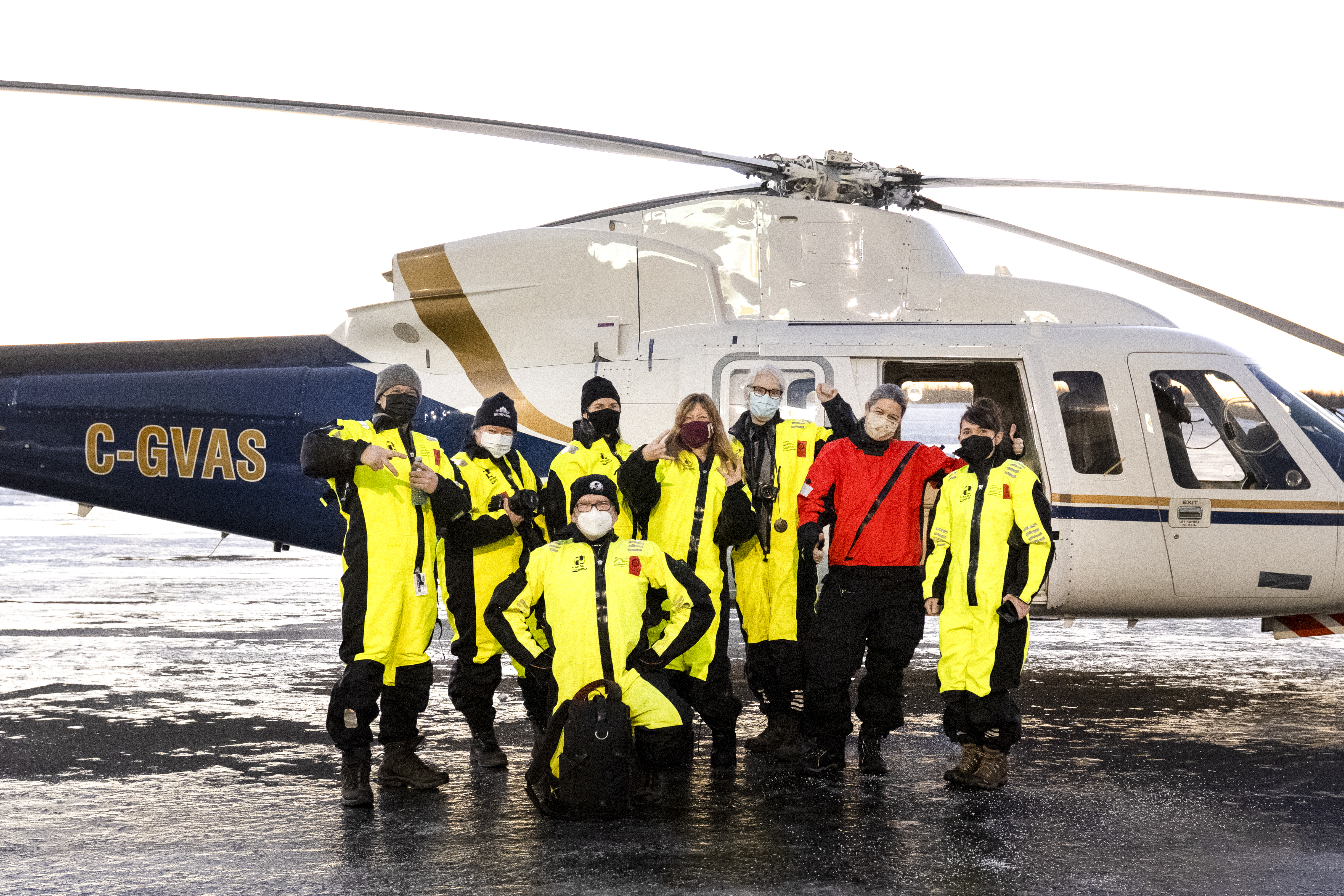 Kattuk’s winter expedition group wearing yellow flight suits beside the helicopter