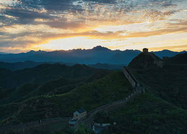 Great wall of china at sunrise with rolling hills.