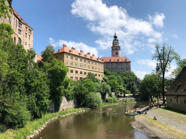 Capture of Český Krumlov Castle with the Vltava River and lush greenery on a sunny day.