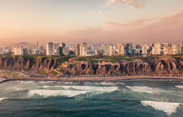 Scenic aerial view of Lima's cliffs and Pacific Ocean coastline during sunset, highlighting urban landscape and natural beauty.