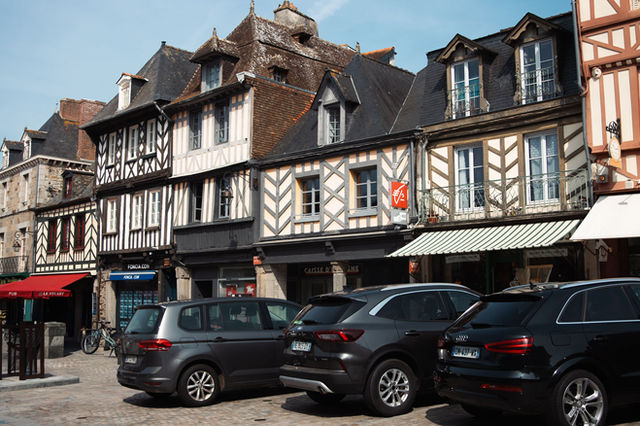 Historical half-timbered houses in Dol-de-Bretagne, Brittany, France on a sunny day with parked cars.