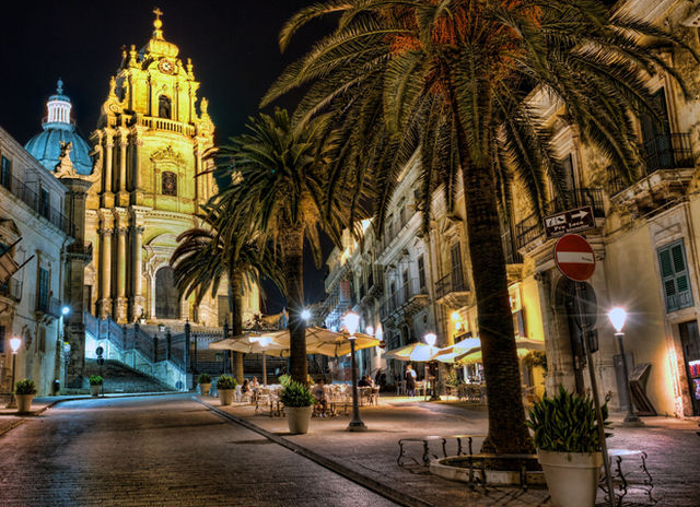 Stunning night view of Duomo di San Giorgio with palm trees in Ragusa, Sicily. Captivating architectural scene.