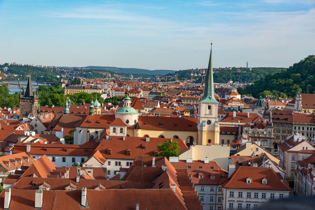 Aerial view of Prague showcasing red rooftops and historic landmarks under a clear blue sky.