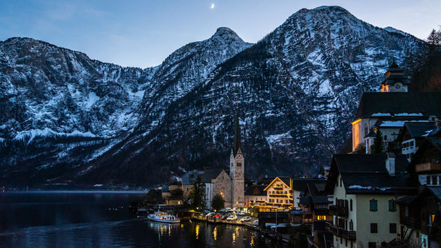 A village nestled by a lake with snowy mountains.