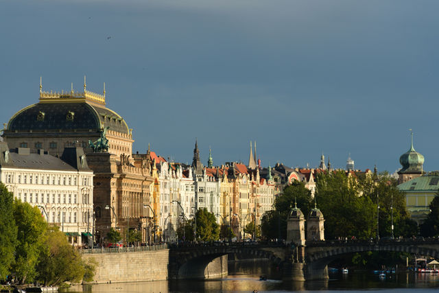 Historic buildings line a river with a bridge.