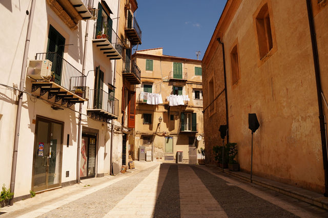 A quiet street scene in Monreale, Sicily, featuring rustic architecture and warm sunlight.