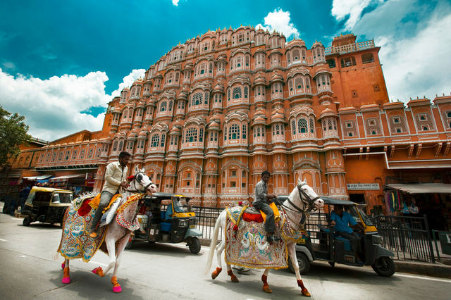 White horses and their riders pass the Hawa Mahal