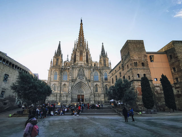 Historic Gothic Cathedral in Barcelona with vibrant crowd and blue sky, showcasing magnificent architecture.