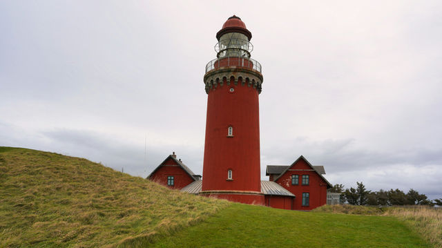 A tall red lighthouse stands on a grassy hill.