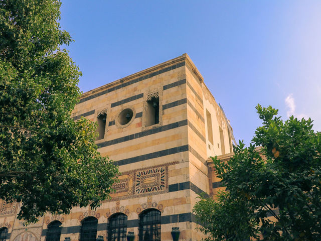 A beautiful historic building with a striped facade in Damascus, Syria, surrounded by lush greenery.