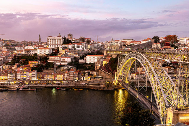 Porto's iconic bridge illuminated at twilight with the historic Ribeira district cascading down the hillside.