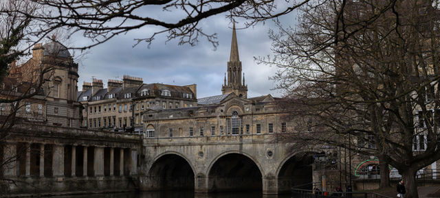 A classic view of Pulteney Bridge in Bath, England with winter trees framing the historic architecture.
