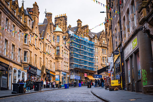 Bustling street scene in Edinburgh with historic architecture and colorful pennant flags.