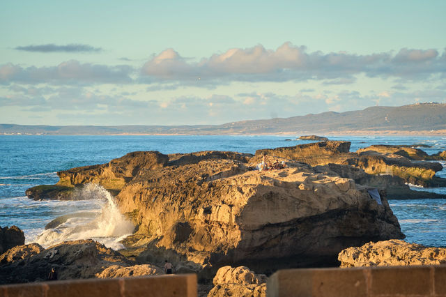 Gorgeous view of the rocky coastline in Essaouira, Morocco at sunset with waves crashing against the rocks.