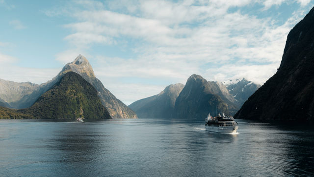A cruise ship sails on a calm lake between mountains.