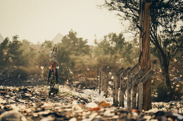 Depicts a woman walking through a field of plastic waste in Burundi, highlighting environmental pollution.