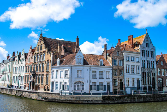Charming townhouses along a canal in Bruges, Belgium under a vibrant blue sky.