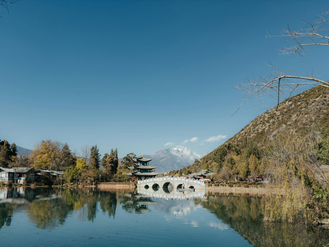 Stone bridge over a calm lake with distant mountains.