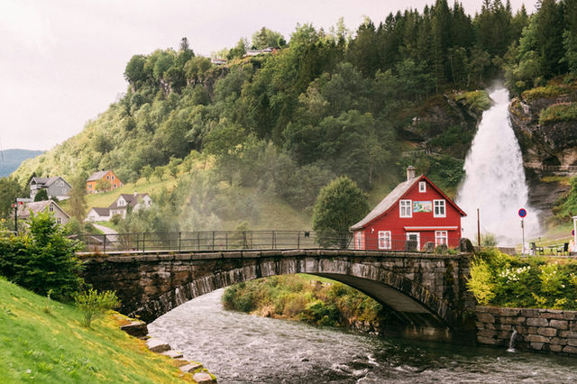 A red house beside a waterfall and stone bridge in a green valley