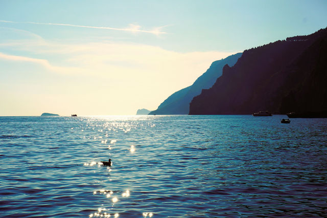 Serene view of Amalfi Coast waters at sunset with distant boats and silhouetted cliffs.