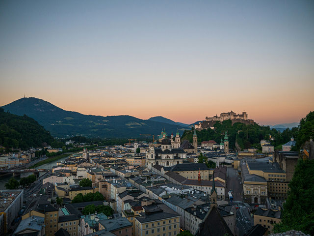 Salzburg city skyline at dusk with mountains and historic castle.
