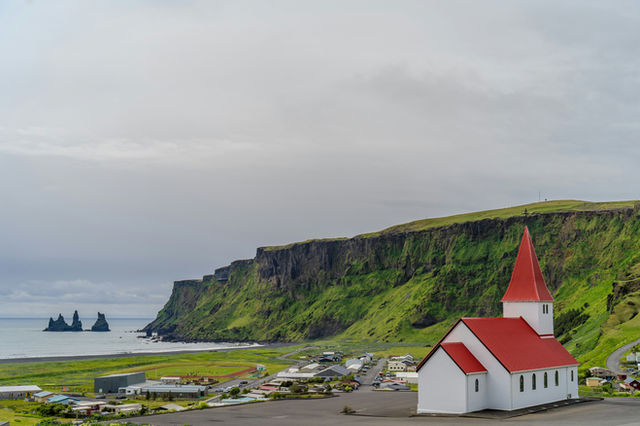 White church with red roof near dramatic cliffs and ocean.