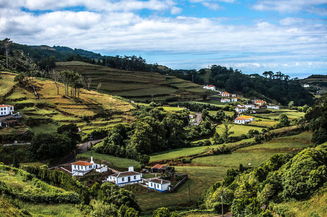 Lush green fields and farmhouses in the Açores, Portugal, under a vibrant sky.